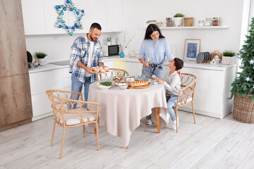 Fototapeta premium Hanukkah celebration and family traditions, parents and son preparing festive dinner with menorah and sufganiyot in a modern kitchen at home