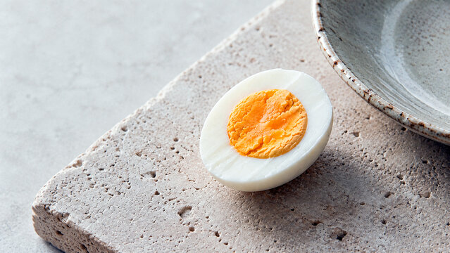 Close up of a halved hard boiled egg on a textured stone surface. Healthy breakfast ingredient with bright yellow yolk. Copy space for text