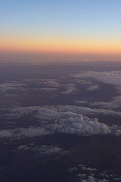 Orange sunset glow above clouds and dark land from airplane