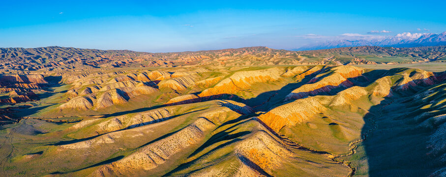 Aerial view of layered rock formations and colorful Danxia landforms under a golden sunset along the S101 highway, Xinjiang, China