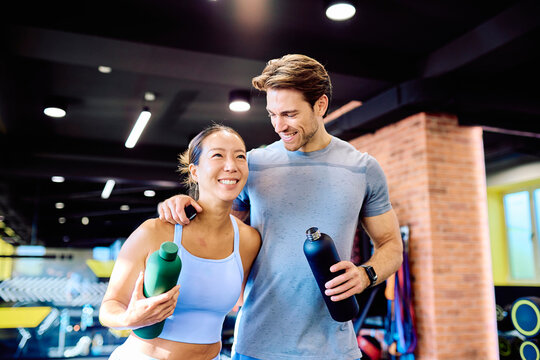 Happy man and woman in sportswear enjoying fitness together. Healthy couple resting with water after gym workout, staying hydrated