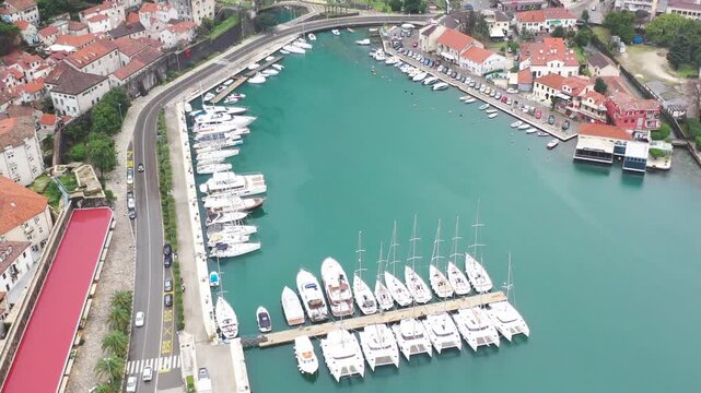 Yacht marina from above, top down aerial view of moored sailboats and motor yachts at pier with seaside road, Montenegro. Yachting and boat charter concept, drone flies over marina