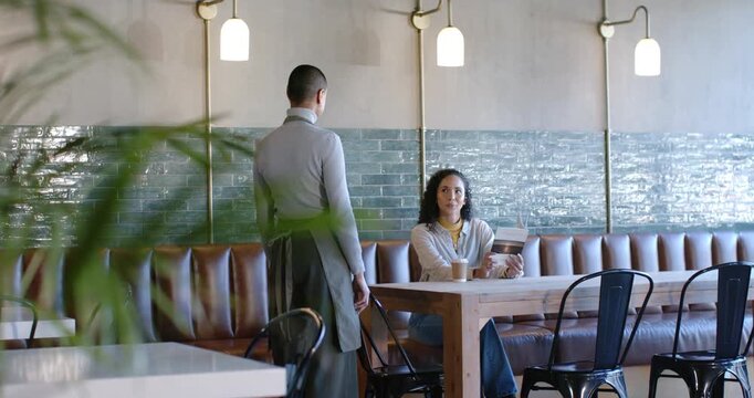 African American women server coming, walking left in cafe as customer reading book holding cup