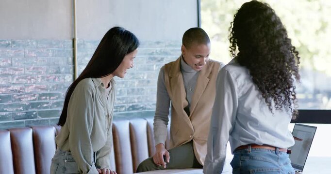 Diverse women team leaning at round table in nook, center woman pointing docs, closing on laptop
