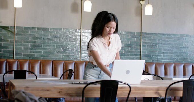 Diverse women at cafe table, Asian bringing laptop and working while woman on phone holding cup