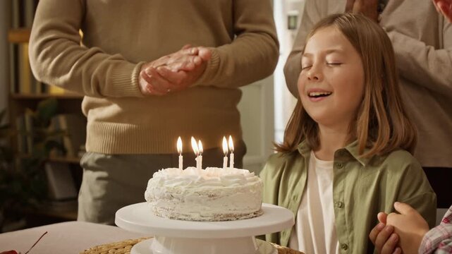 Caucasian girl making wish and blowing out candles on birthday cake while family claps. Clip suitable for family lifestyle advertising, festive confectionery promotions and insurance campaigns