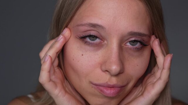 Young woman touches her eye area and shows false eyelashes or eyelash extensions in close-up, focusing on the finished beauty result and lash definition