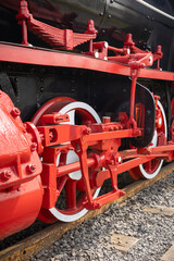 Close-up of red wheels, pistons, and mechanical parts of an old steam locomotive train on tracks. © MARCELO