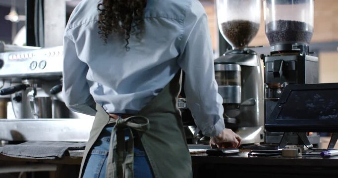 Barista is dosing grinder, tamping portafilter, pulling espresso, steaming milk at bar for orders