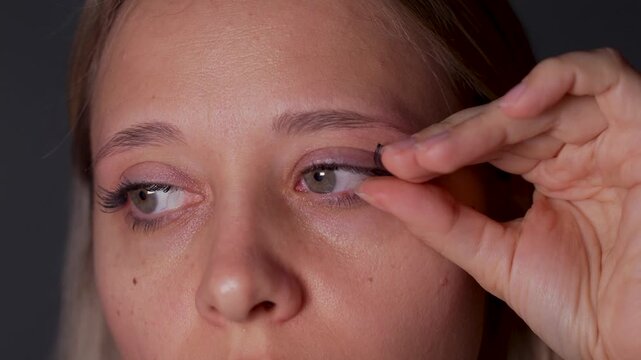 Young woman carefully removes false eyelashes from one eye with her fingers, showing the beauty removal process in a close-up skincare and makeup routine