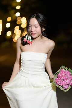Young woman in elegant white dress holding bouquet of pink roses at night