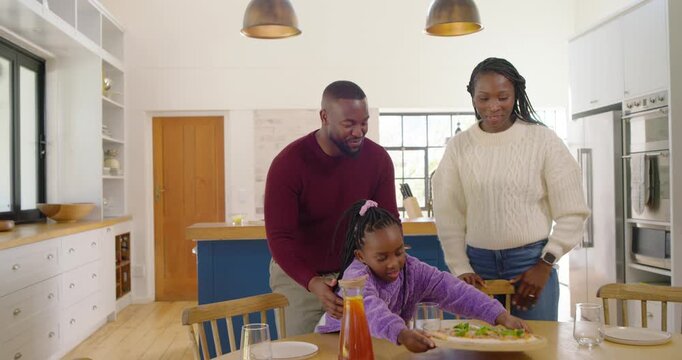 African American family bringing pizza on board to dining table after timer to eat, opening sauce