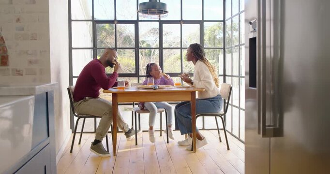African American family sitting at table sunlight drawing mom feeding child, dad lifting juice