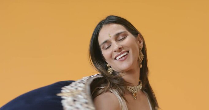 Indian woman modeling on cue in orange studio, draping dupatta, showing necklace earrings bindi