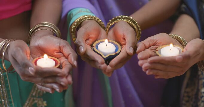 Three cupped hands are holding small lit lamps, steadying and aligning them during ritual offering