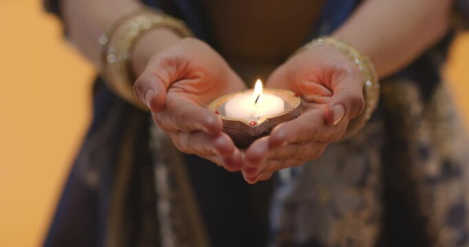 Ritual is starting, hands are cupping lit earthen diya and steadying flame for offering