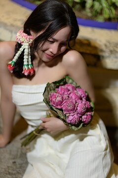Woman holding a bouquet of pink flowers with short dark hair and floral hair accessory, indoor setting