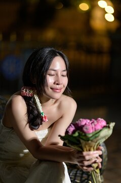 Young woman holding a bouquet of pink roses with a joyful expression outdoors at night