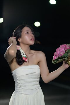 Elegant young woman in white strapless dress holding pink hydrangea flowers at night