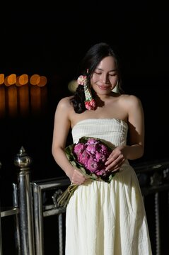 Woman in white dress holding pink flower bouquet outdoors at night with city lights background