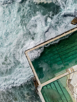 Ocean swimming pool with waves breaking on sunny day from vertical top down aerial view. Bondi Icebergs is a famous swimming pool at Bondi Beach in Sydney, Australia.