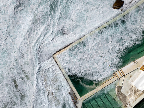 Ocean swimming pool with big waves breaking on sunny day from a high top down aerial view. Bondi Icebergs is a famous swimming pool at Bondi Beach in Sydney, Australia.