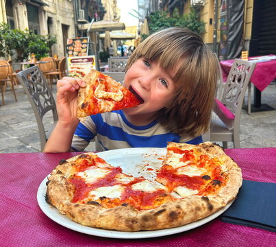Portrait of a boy and pizza. A 7-year-old child sits outside at a cafe in Italy eating a Neapolitan pizza Margherita. Travel with children, fast food in Italy