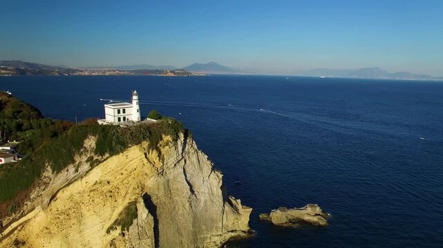 Aerial retreat from Capo Miseno lighthouse and rocky cliffs Italy