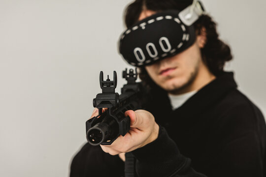 Man wearing virtual reality headset aiming AR-15 rifle controller in VR training simulation
