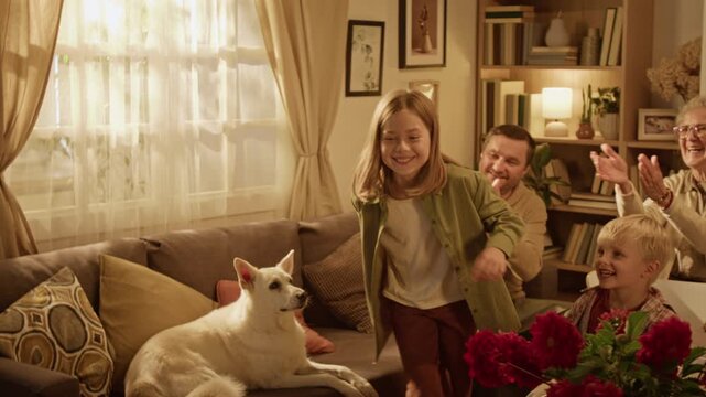 Caucasian woman playing charades game with multigenerational family applauding happy girl. Perfect for advertising social bonding, indoor leisure, and home entertainment