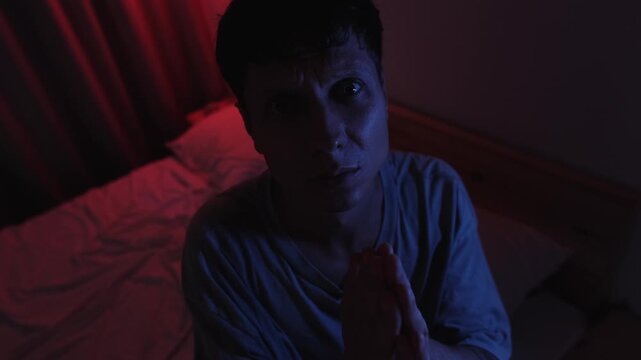 Desperate man praying with clasped hands and looking directly into the camera, pleading for divine help and forgiveness in a powerful direct address scene with blue light and red low key background