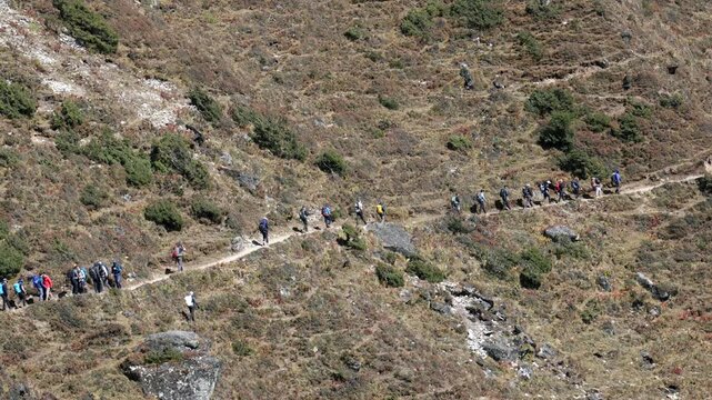 Large group of tourists and porters walking in long line on narrow footpath during an expedition in remote high altitude mountains of sagarmatha national park in nepal. Everest base camp trek