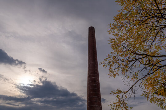 Tall chimney against a cloudy sky with autumn leaves visible on a nearby tree