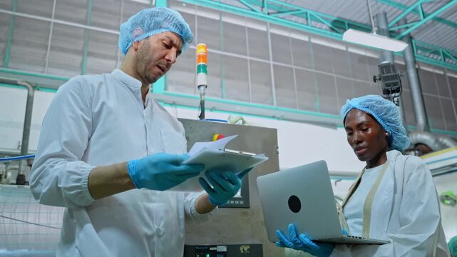 Factory workers review production data beside automated machinery in a hygienic beverage packaging facility, supporting quality control, safety, and efficient manufacturing operations.