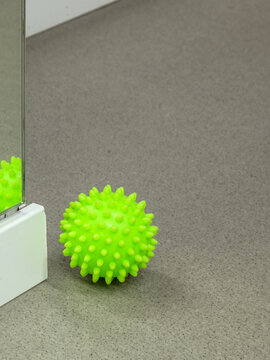 Bright green spiky massage ball on a grey textured floor near a mirror. This equipment represents physical therapy, muscle recovery, and sensory integration for health and wellness concepts.