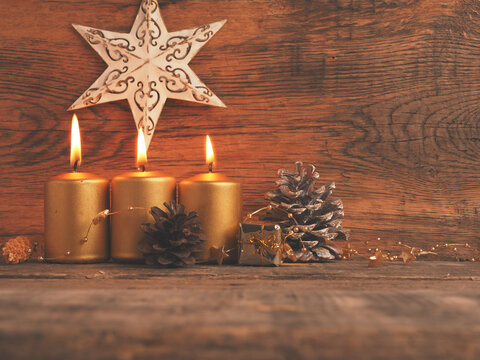 Three Golden Advent candles on a rustic wooden background, third Advent candle is burning