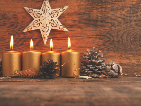 Four Golden Advent candles on a rustic wooden background, fourth Advent candle is burning