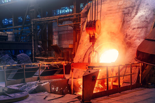 Molten metal pouring from furnace during foundry casting at metallurgical plant.