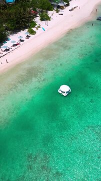 Aerial floating dome near shoreline, white dome in shallow turquoise water, lined umbrellas and sunbeds on white sand, palm fringe and resort vibe, drone hospitality shot, vertical video