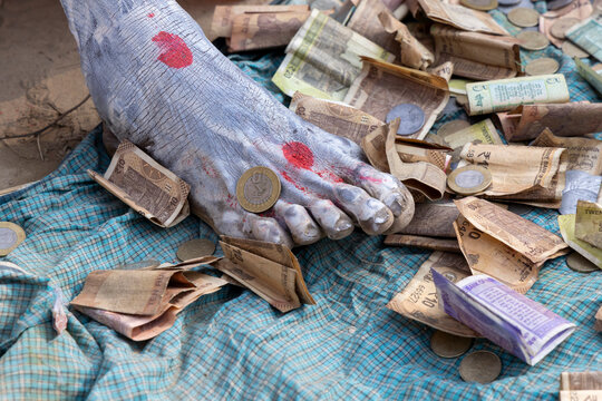 Close-up of an ash covered foot with red marks resting on a checked cloth among banknotes and coins, Prayagraj, India