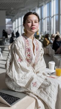 Young asian female in embroidered dress enjoying coffee at sunlit cafe