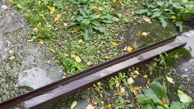 Rainwater flows through a metal drainage channel near a house, construction surveillance camera and stormwater management footage