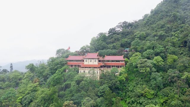 Static aerial hold on a pagoda-style Buddhist temple with red tile roofs on a forested slope, misty valley and hills behind, Yen Tu, Quang Ninh, Vietnam