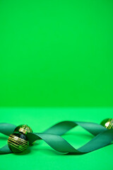 Green Christmas background with shiny baubles and curved satin ribbon at the bottom. Selective focus, softly blurred decorations and large copy space for festive greetings and holiday designs. © ольга дубровная
