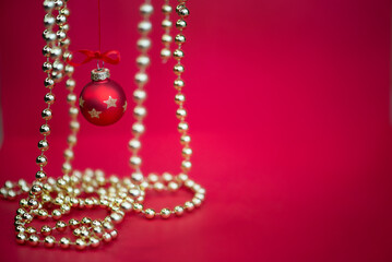 Red Christmas baubles and hanging golden bead garlands on a festive red background. Selective focus and blurred decorations create depth, with ample copy space for holiday greetings and advertising. © ольга дубровная