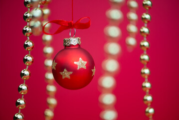 Red Christmas baubles and hanging golden bead garlands on a festive red background. Selective focus and blurred decorations create depth, with ample copy space for holiday greetings and advertising. © ольга дубровная