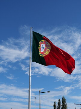 Large flag of Portugal waving in bright blue sky with a few clouds vertical photo