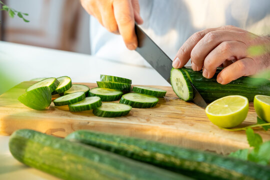 Hands slicing fresh cucumber into rounds on wooden cutting board