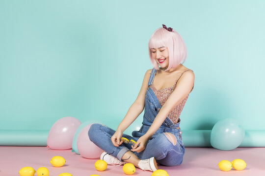 Young woman with pink hair sitting with lemons and balloons in a studio