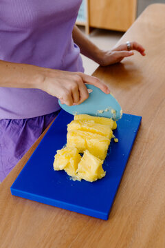 Woman using a kitchen spatula to chop butter on a blue cutting board.